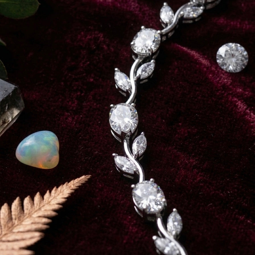 Silver leaf-shaped jewelry piece on a dark fabric background with an opal stone and leaves.