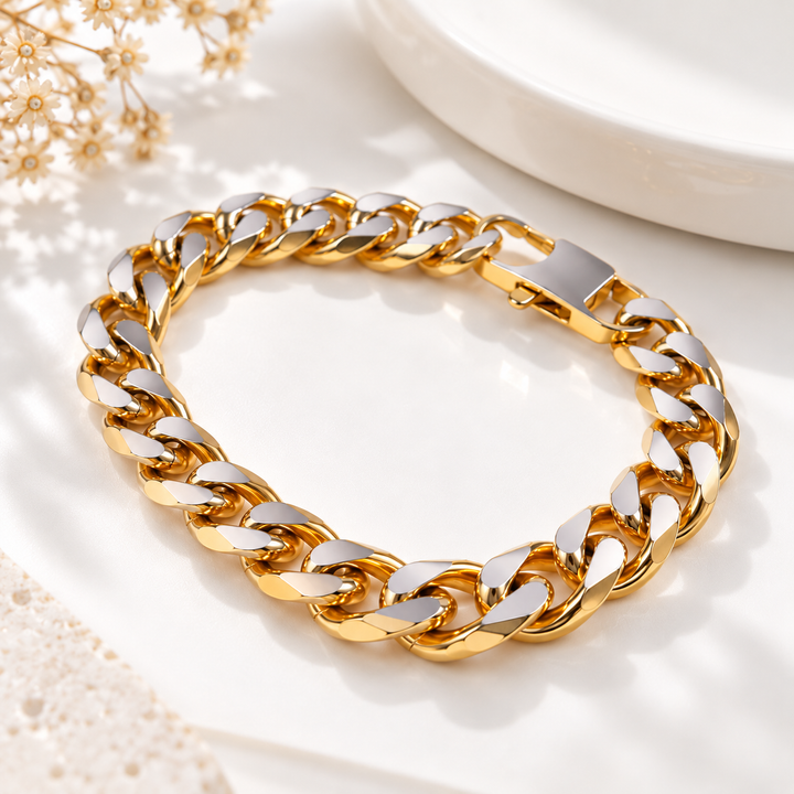 A thick gold and silver chain bracelet arranged in an oval on a white surface with soft decorative props.