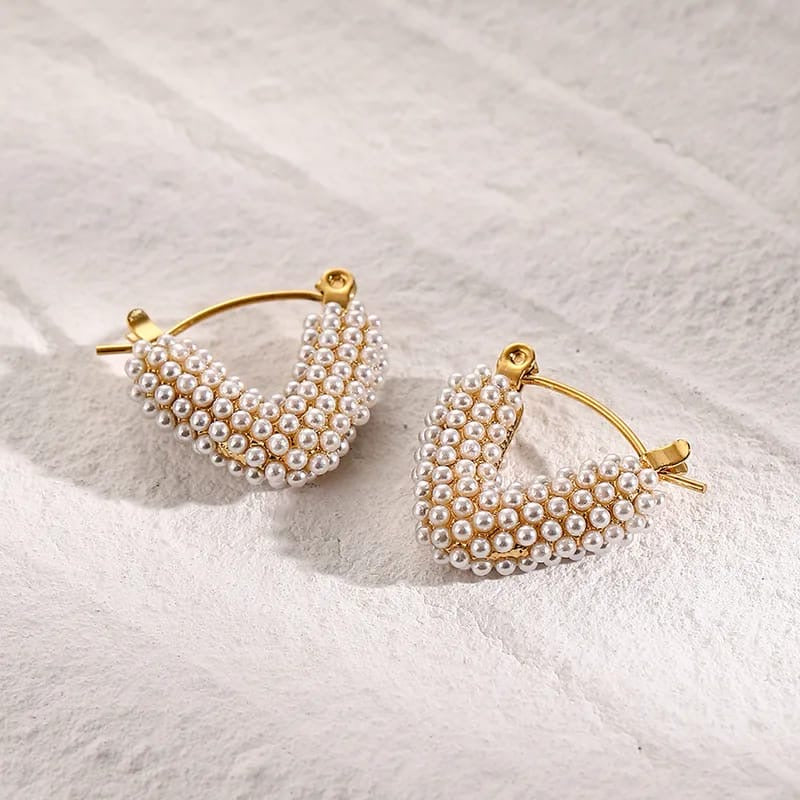 Pair of gold hoop earrings with pearl beads on a textured white surface