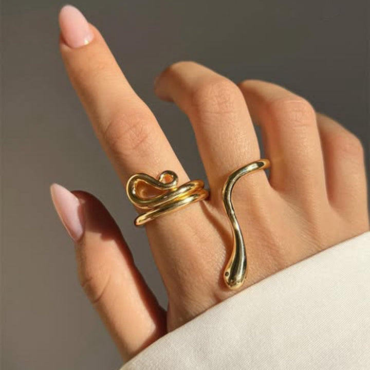 Gold snake-shaped ring on a hand against a neutral background