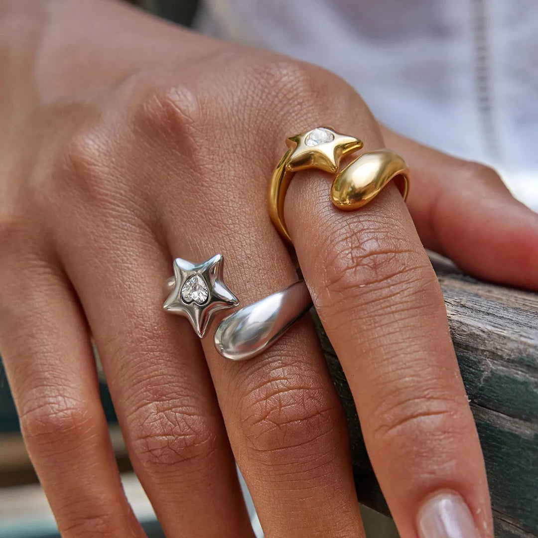 Close-up of a hand wearing two star-shaped rings, one gold and one silver, on a blurred background.