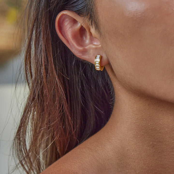 Close-up of a person wearing gold hoop earrings with blurred background