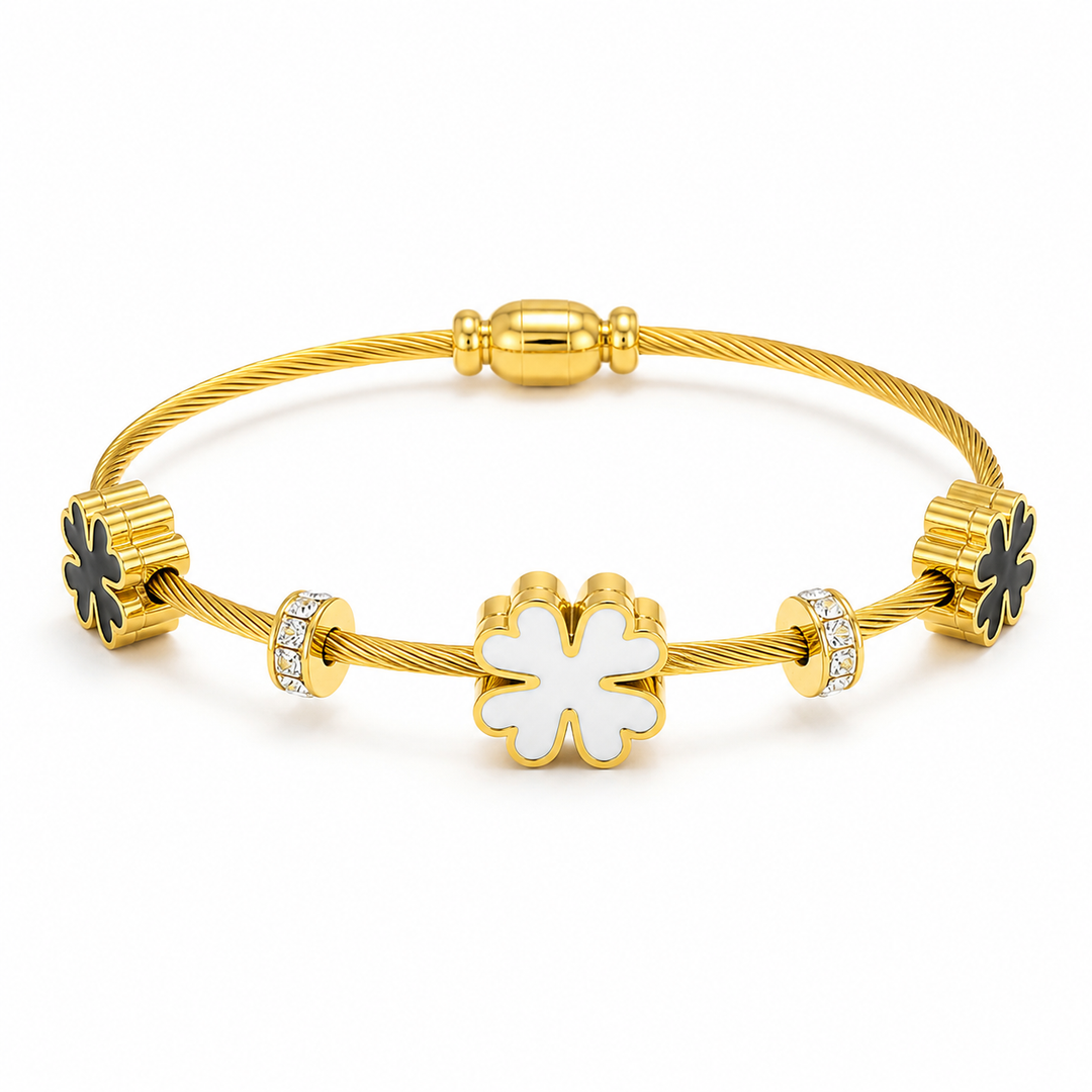 A gold cable bangle bracelet featuring a central white enamel four-leaf clover charm, flanked by textured gold clover charms with black enamel accents and small clear crystal-set beads.