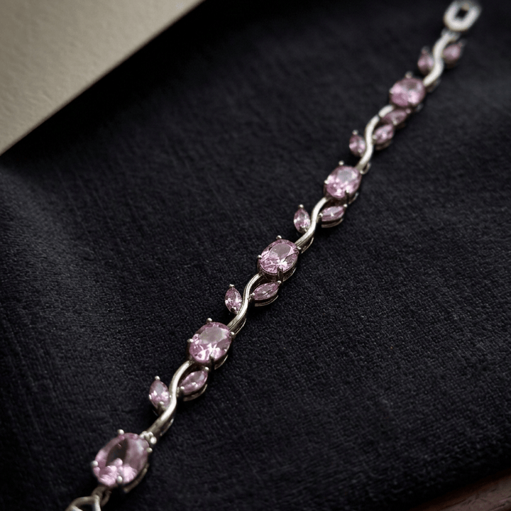 Pink gemstone bracelet on a dark fabric background with a brand card.