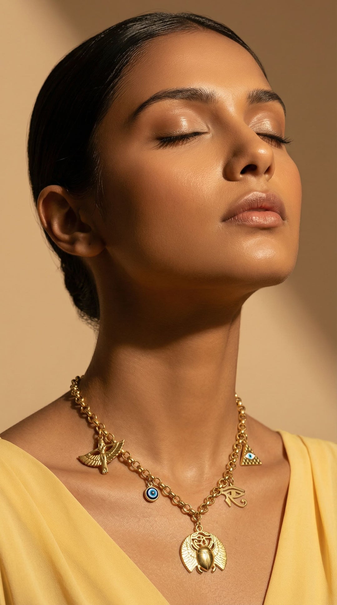 Woman wearing a gold necklace with various pendants against a beige background