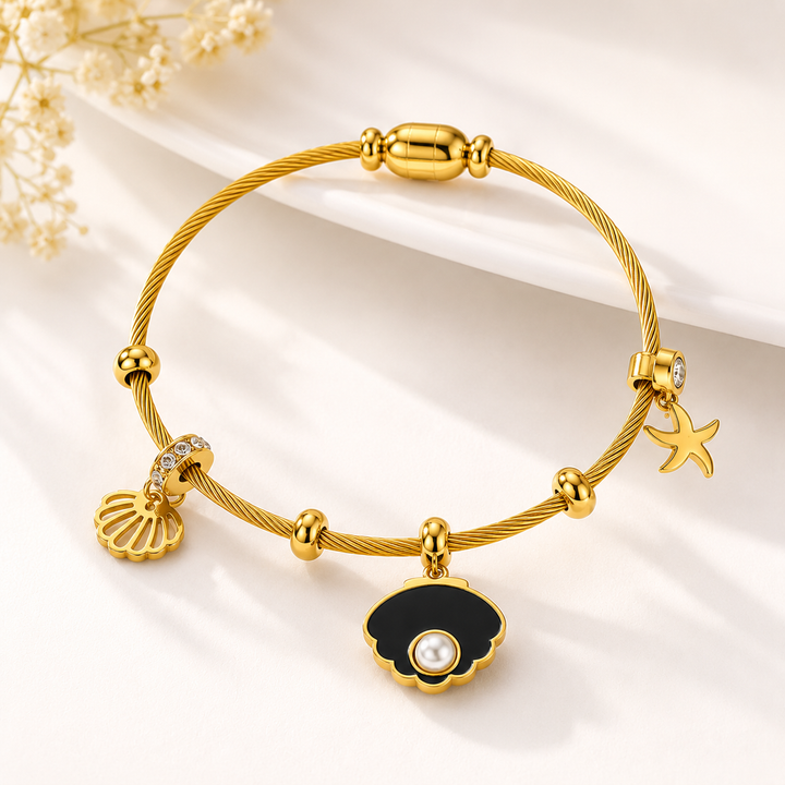 A gold-plated cable bracelet featuring a clam shell charm with a white pearl center, a seashell charm, a starfish charm, and a rhinestone-accented charm, displayed on a clean white background with soft shadows.