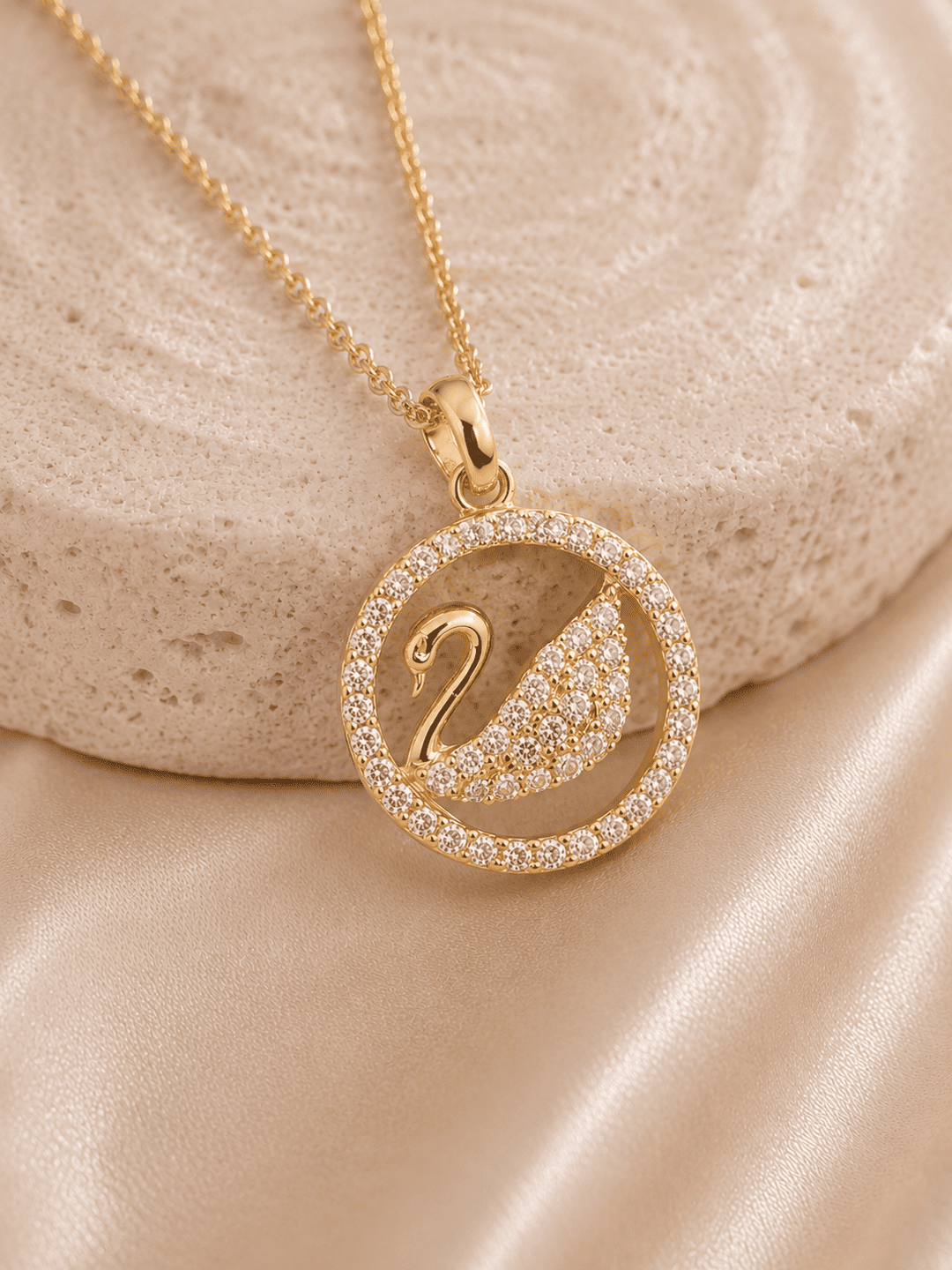 Gold necklace with a swan pendant on a beige stone surface