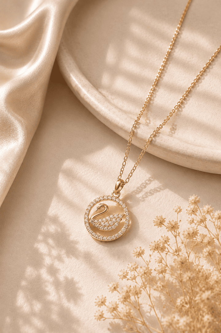 Gold necklace with a swan pendant on a beige fabric background