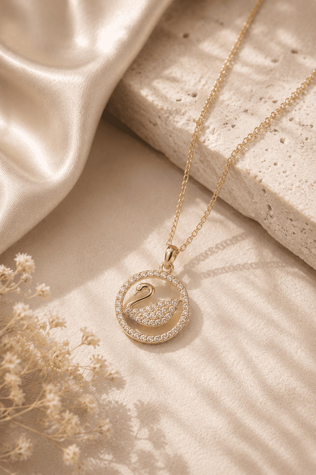 Gold necklace with a circular pendant on a textured surface with fabric and flowers.