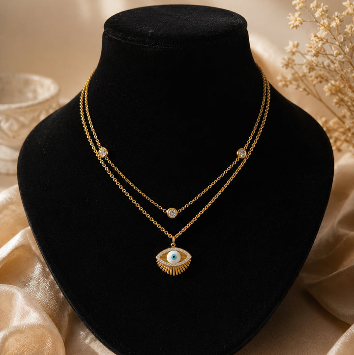 Gold necklace with an eye pendant on a black velvet stand with a soft beige background.