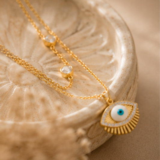 Gold necklace with an eye-shaped pendant on a textured beige surface