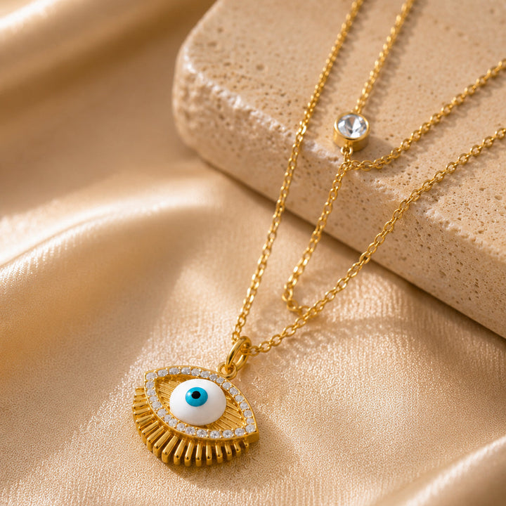 Gold necklaces with eye-shaped pendants on a beige fabric background