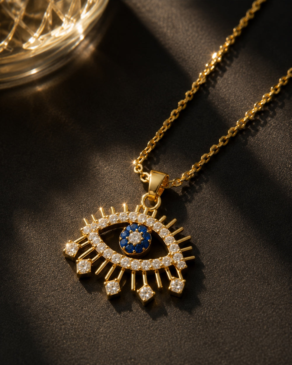 Gold necklace with an eye-shaped pendant featuring a blue center on a dark surface.