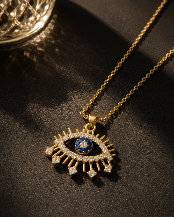 Gold necklace with an eye-shaped pendant on a dark surface