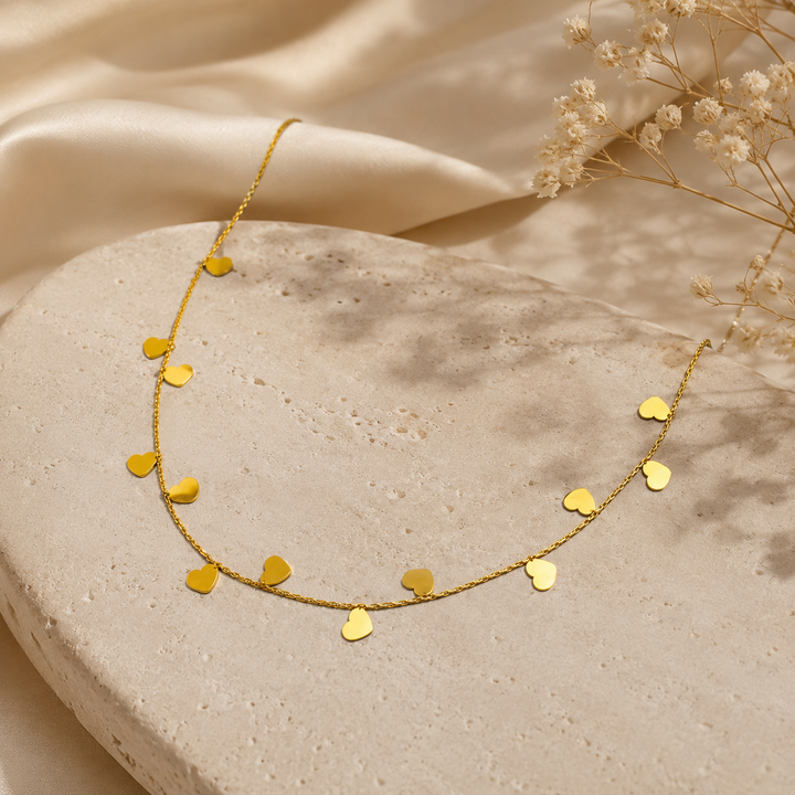 Gold heart-shaped necklace on a stone surface with dried flowers