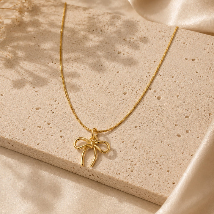 Gold necklace with a bow pendant on a beige stone surface