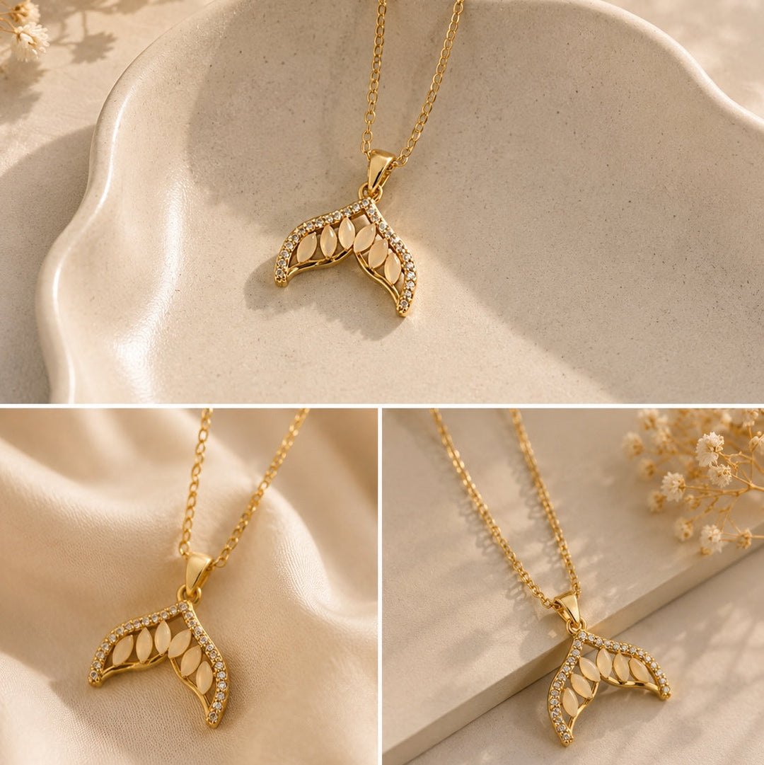 Gold necklace with leaf-shaped pendant on a beige surface with dried flowers.