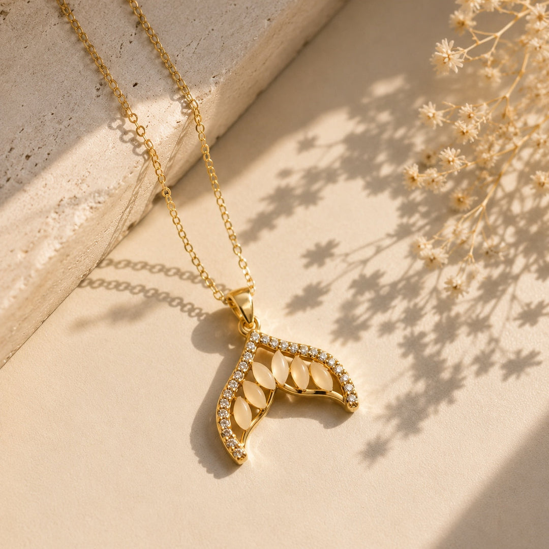 Gold necklace with a leaf-shaped pendant on a light background