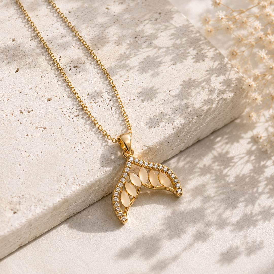 Gold necklace with a leaf-shaped pendant on a light stone surface.