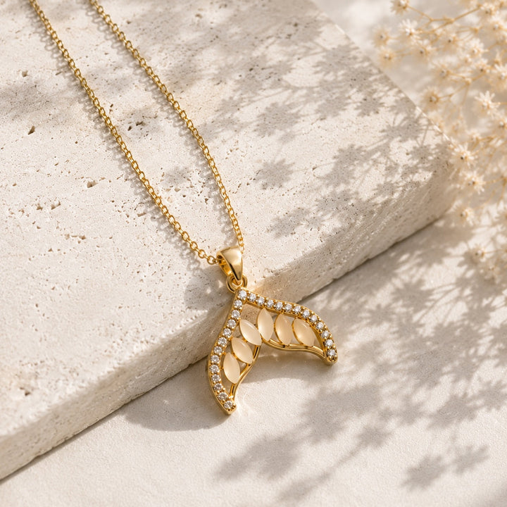 Gold necklace with a leaf-shaped pendant on a light stone surface.