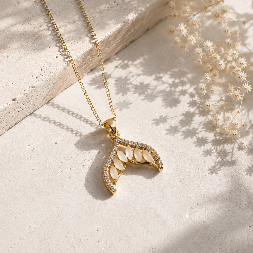 Gold necklace with a decorative pendant on a light surface with dried flowers.
