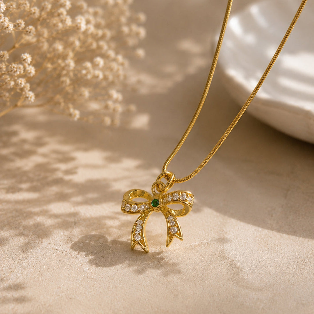 Gold necklace with a bow-shaped pendant on a beige surface with dried flowers.
