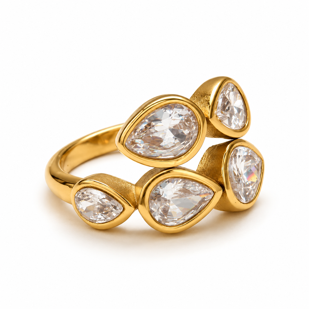 A gold ring featuring four teardrop-shaped clear gemstones in bezel settings, arranged in two overlapping rows on a clean white background.