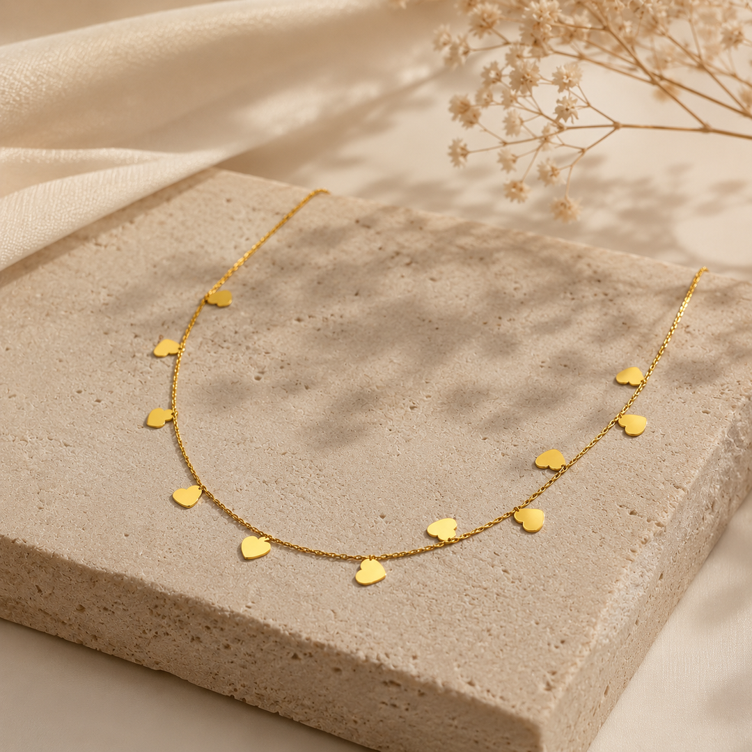 Gold necklace with heart-shaped pendants on a textured surface with dried flowers.