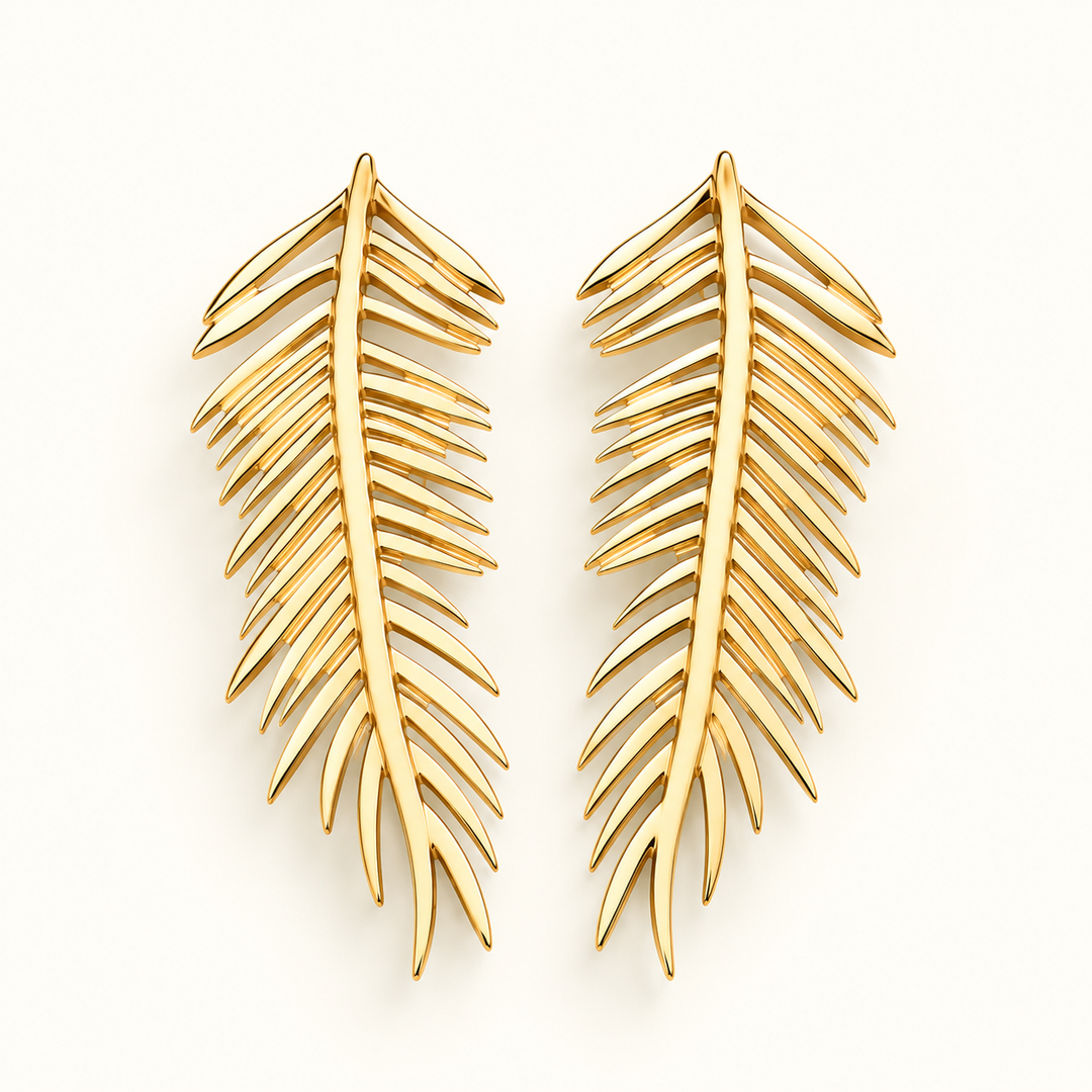 A pair of gold-toned leaf-shaped earrings with a polished finish, displayed on a clean off-white background.
