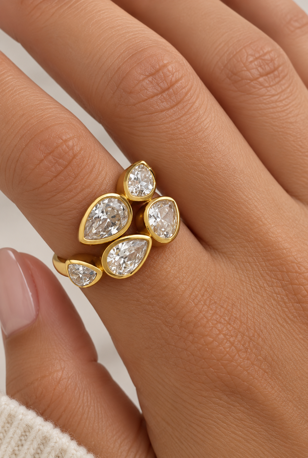 A close-up of a hand wearing a gold ring with five pear-cut clear gemstones in a clustered leaf-like design.