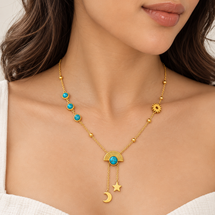 A close-up of a woman wearing a delicate gold necklace with turquoise blue stones, a crescent moon, a star, and a sun pendant.