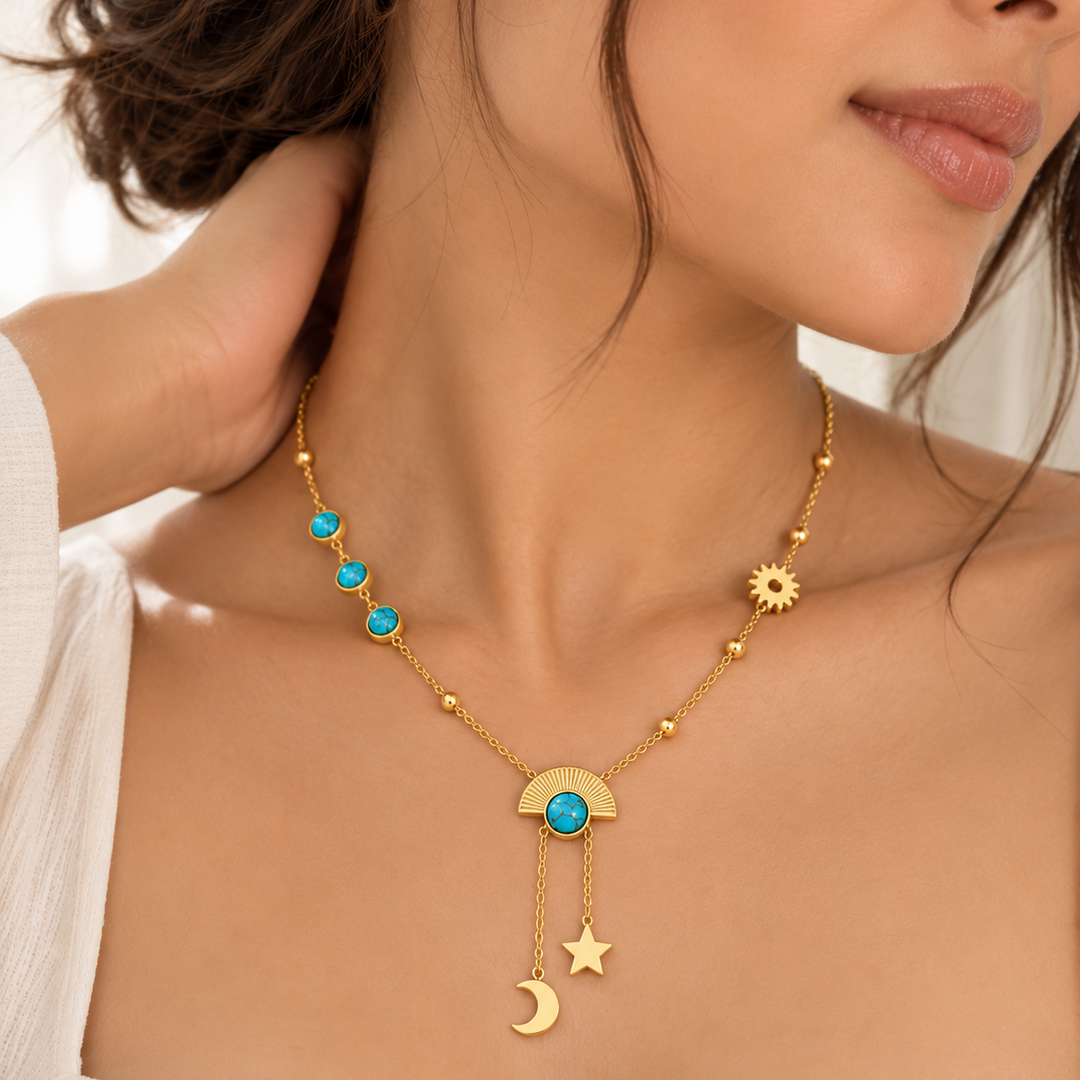 A close-up lifestyle shot of a model wearing a delicate gold necklace with celestial charms. The necklace features a gold crescent moon and star pendant, a gold sunflower charm, and small gold beads accented with vibrant turquoise blue stones.