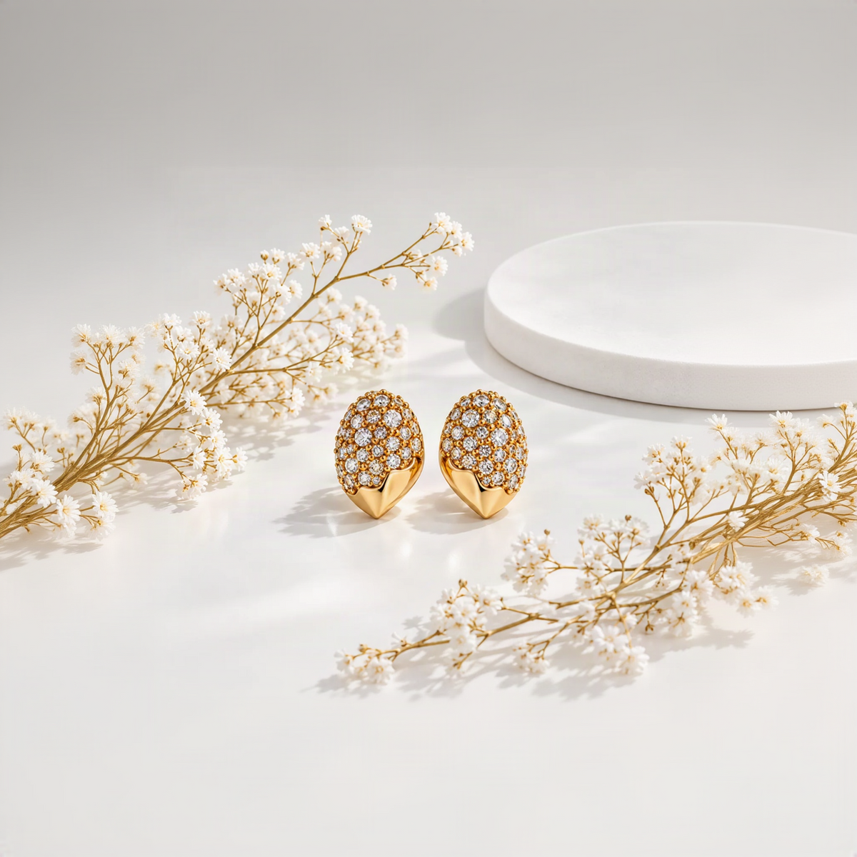 Gold-tone pavé stud earrings with sparkling clear stones, styled on a white surface with baby's breath flowers and a marble pedestal – Élan d'Or anti-tarnish demi-fine jewellery