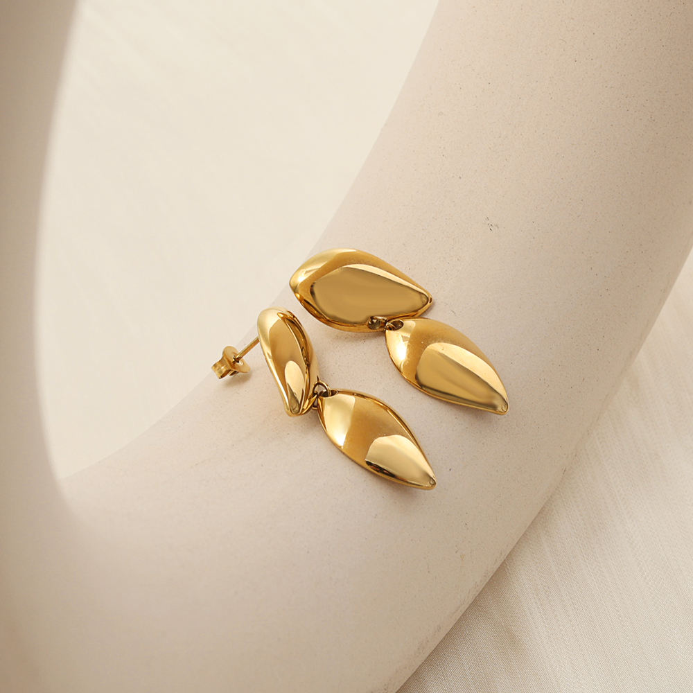 A pair of gold drop earrings with teardrop-shaped dangling pieces, displayed on a cream-colored jewelry stand.