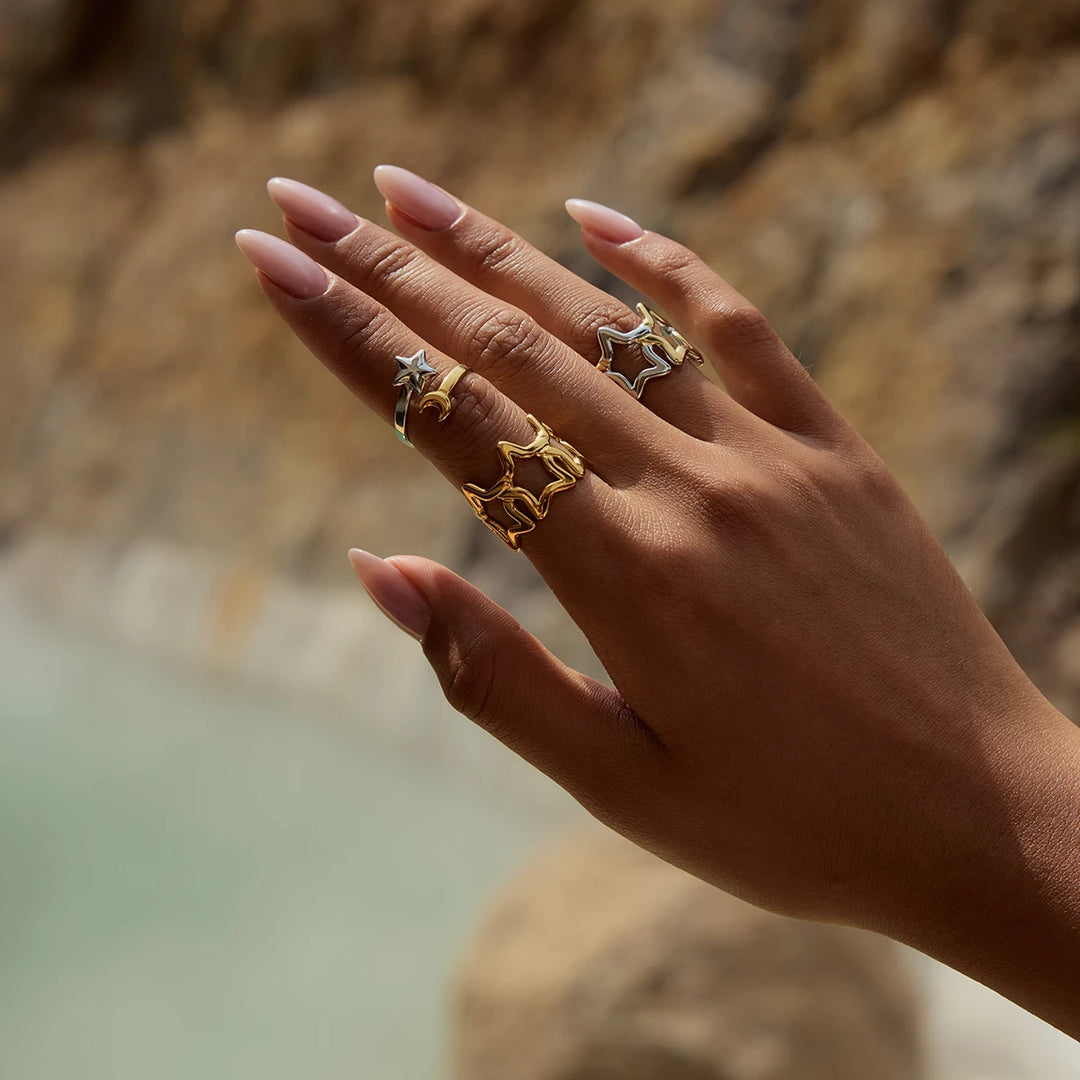 Hand wearing multiple gold rings with a blurred natural background