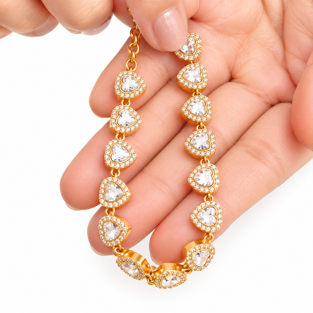 A gold heart-link bracelet with clear heart-shaped crystals, held in a person&