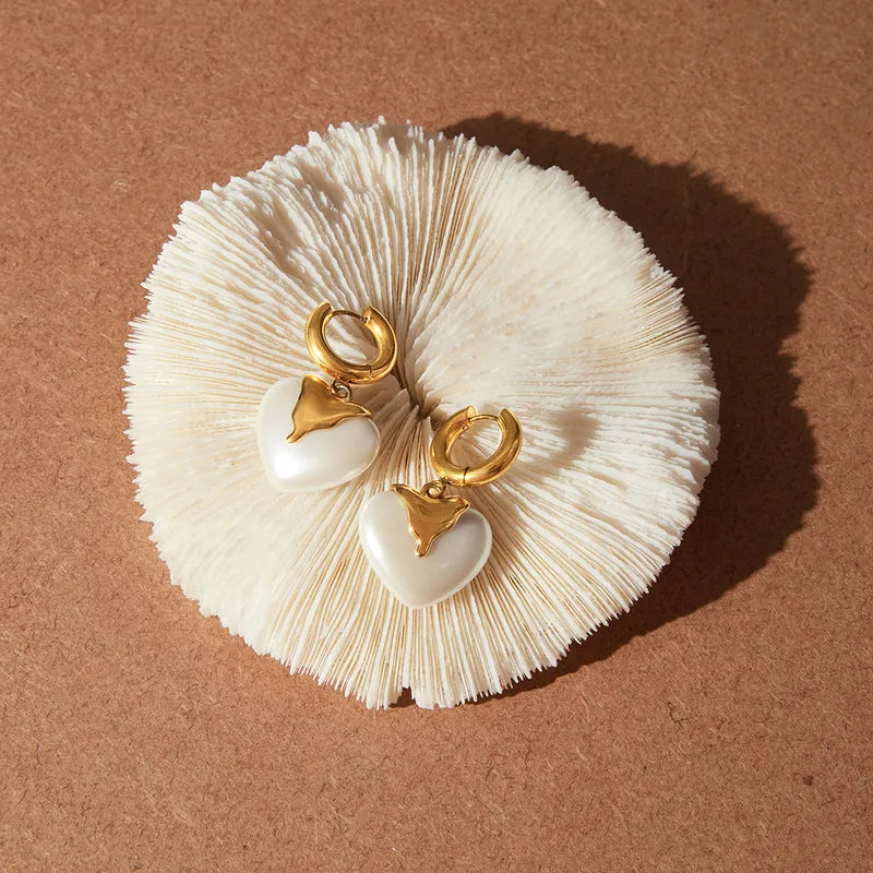 Pair of earrings with gold hearts on a textured beige surface