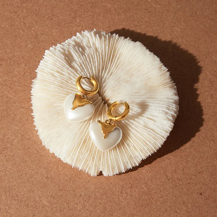 Pair of earrings with gold hearts on a textured beige surface