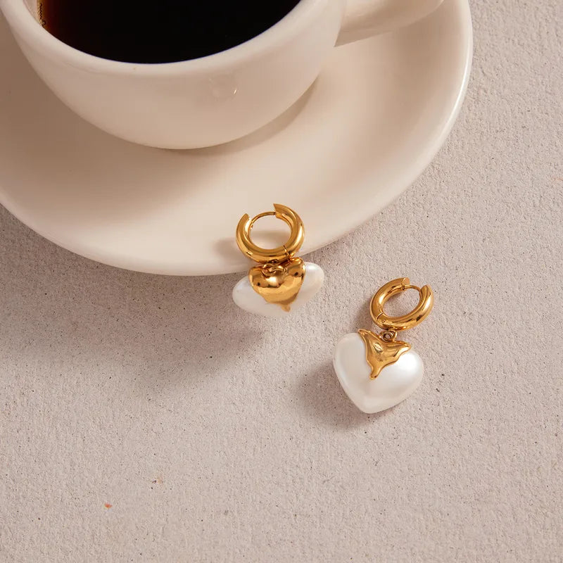 Gold and pearl earrings on a light surface with a cup of coffee in the background