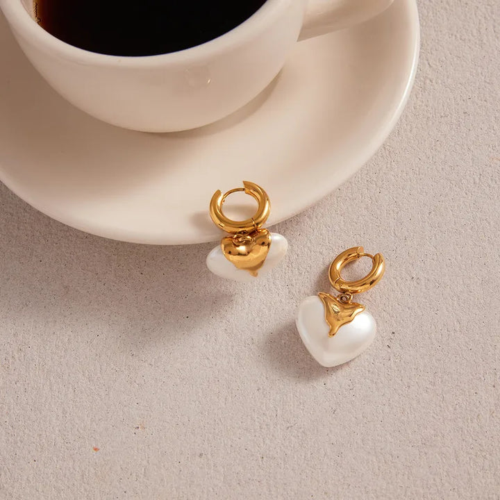Gold and pearl earrings on a light surface with a cup of coffee in the background