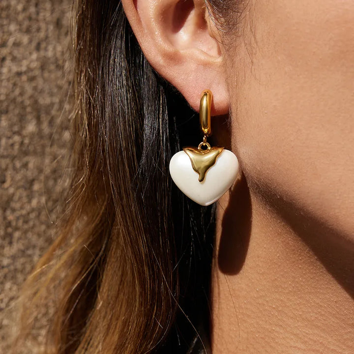 Close-up of a person wearing a gold and white heart-shaped earring against a neutral background.