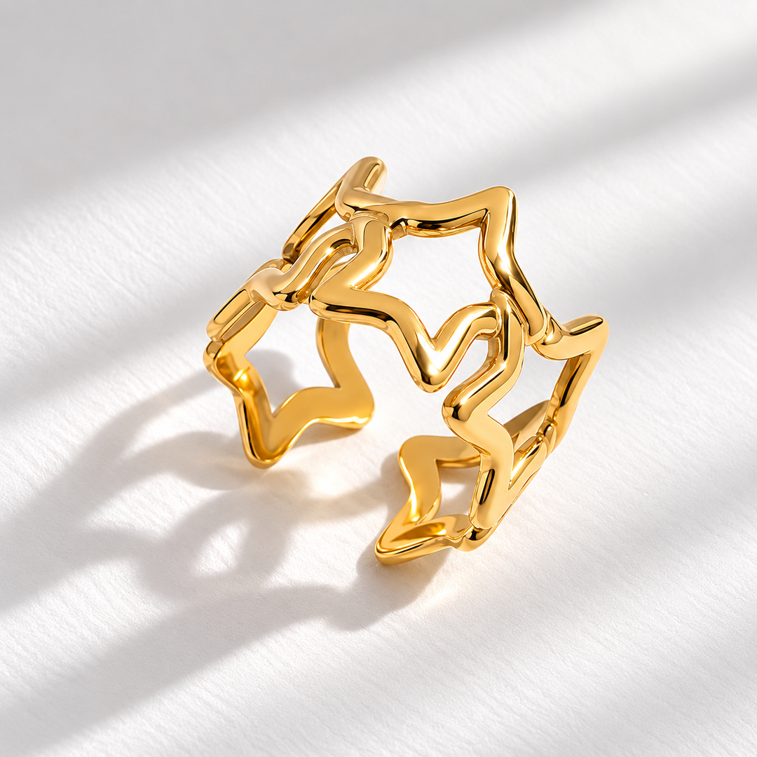 A gold open ring with an abstract, wavy star-like outline, photographed on a white textured surface with soft diagonal shadows.