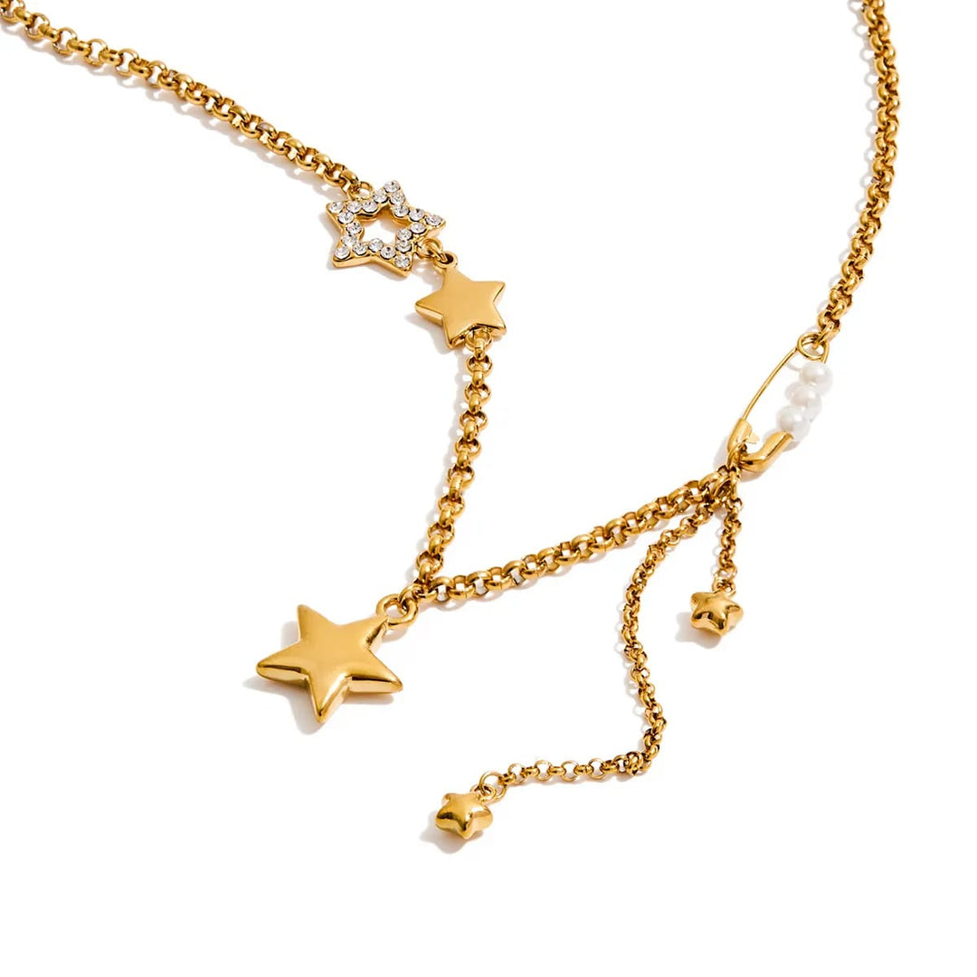 Gold-toned multi-strand chain necklace with star charms, a rhinestone-embellished star, a small white pearl bead, and a safety-pin style connector, shown on a white background.