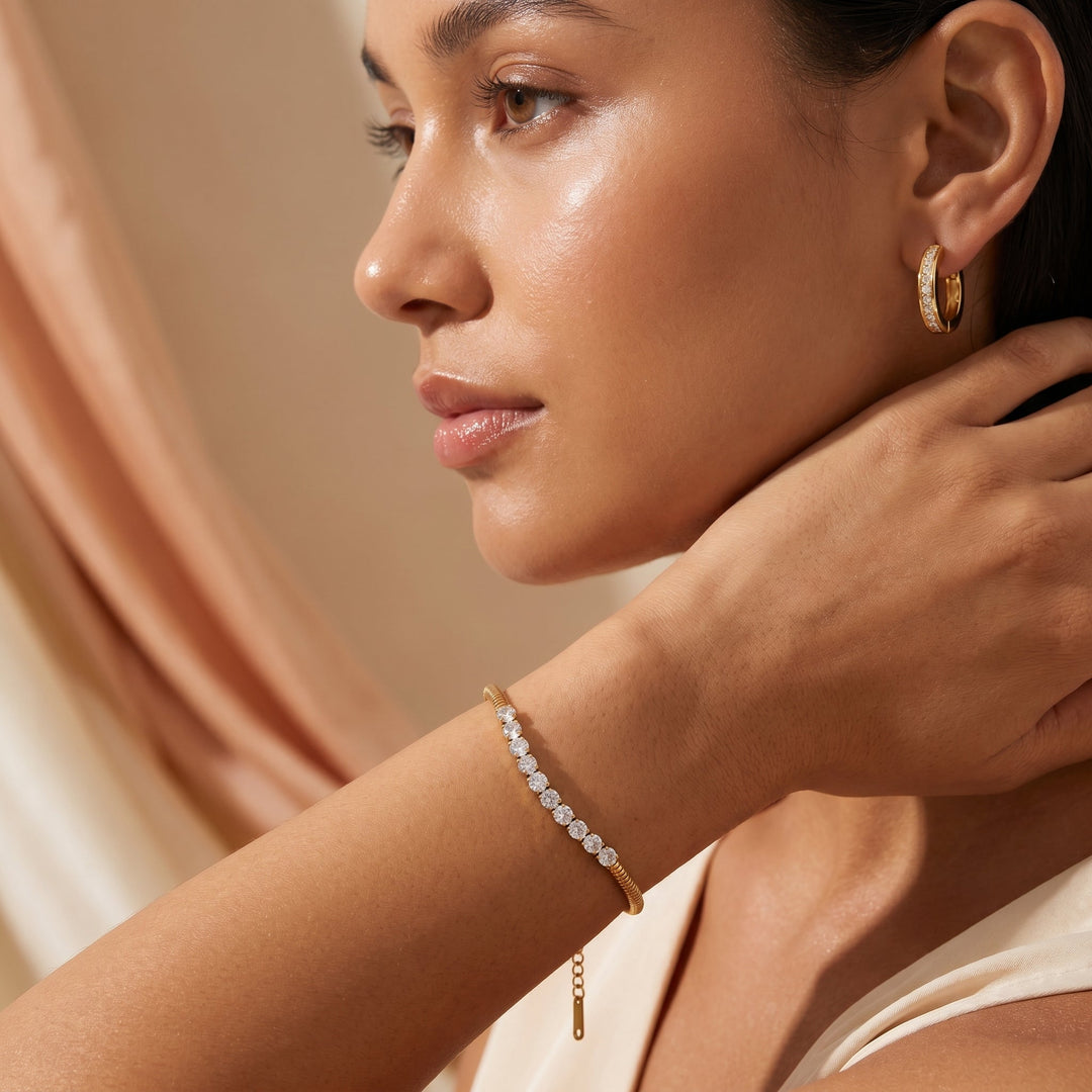 Woman wearing gold hoop earrings and bracelet against a neutral background