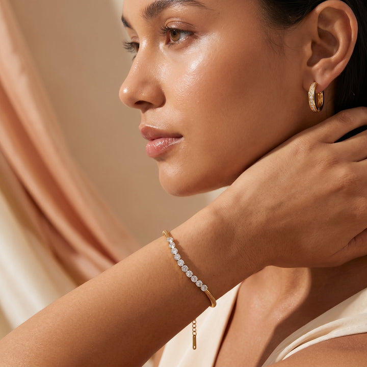 Woman wearing gold hoop earrings and bracelet against a neutral background