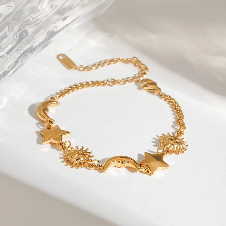 Gold bracelet with star and sun designs on a white surface