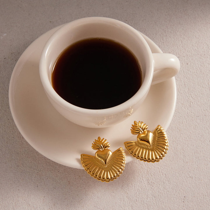 White cup of coffee on a saucer with gold earrings on a light gray background
