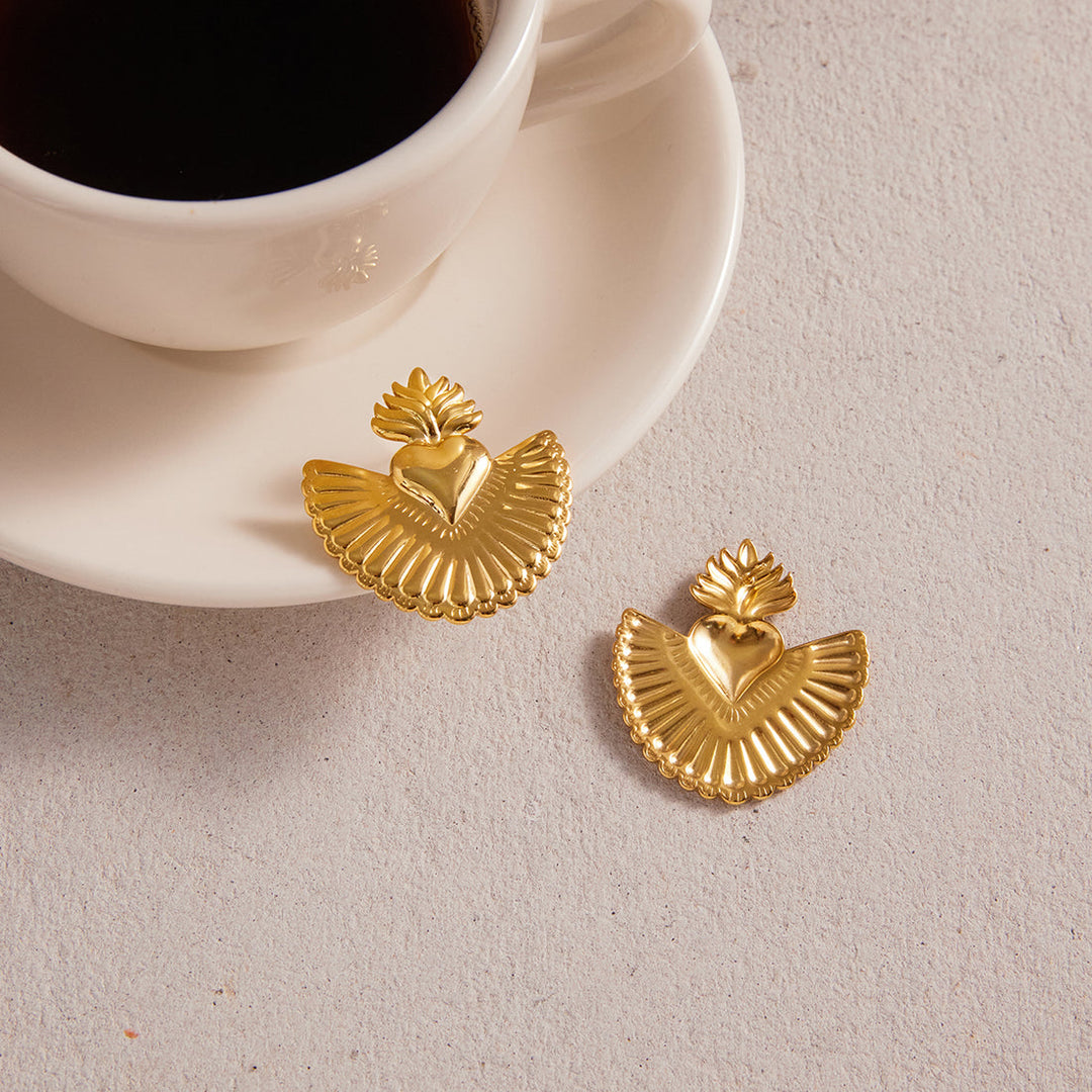 Gold earrings on a light surface with a cup of coffee in the background