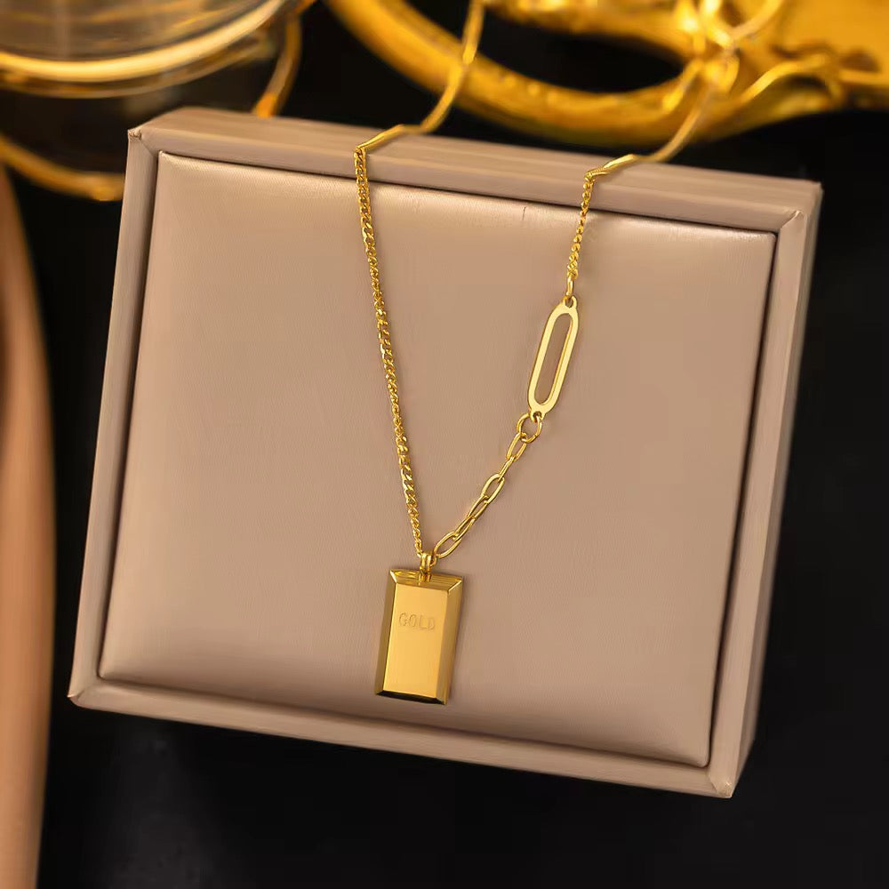 Gold necklace with a rectangular pendant on a beige box