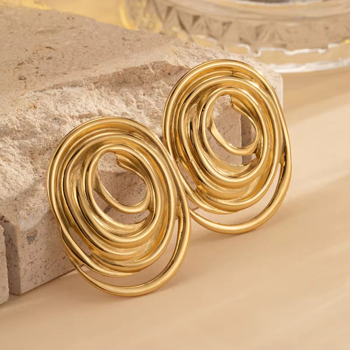 Gold spiral earrings on a textured beige surface